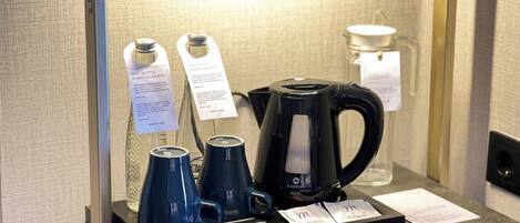 A coffee station with a black coffee maker, two blue cups, and two tags with messages.
