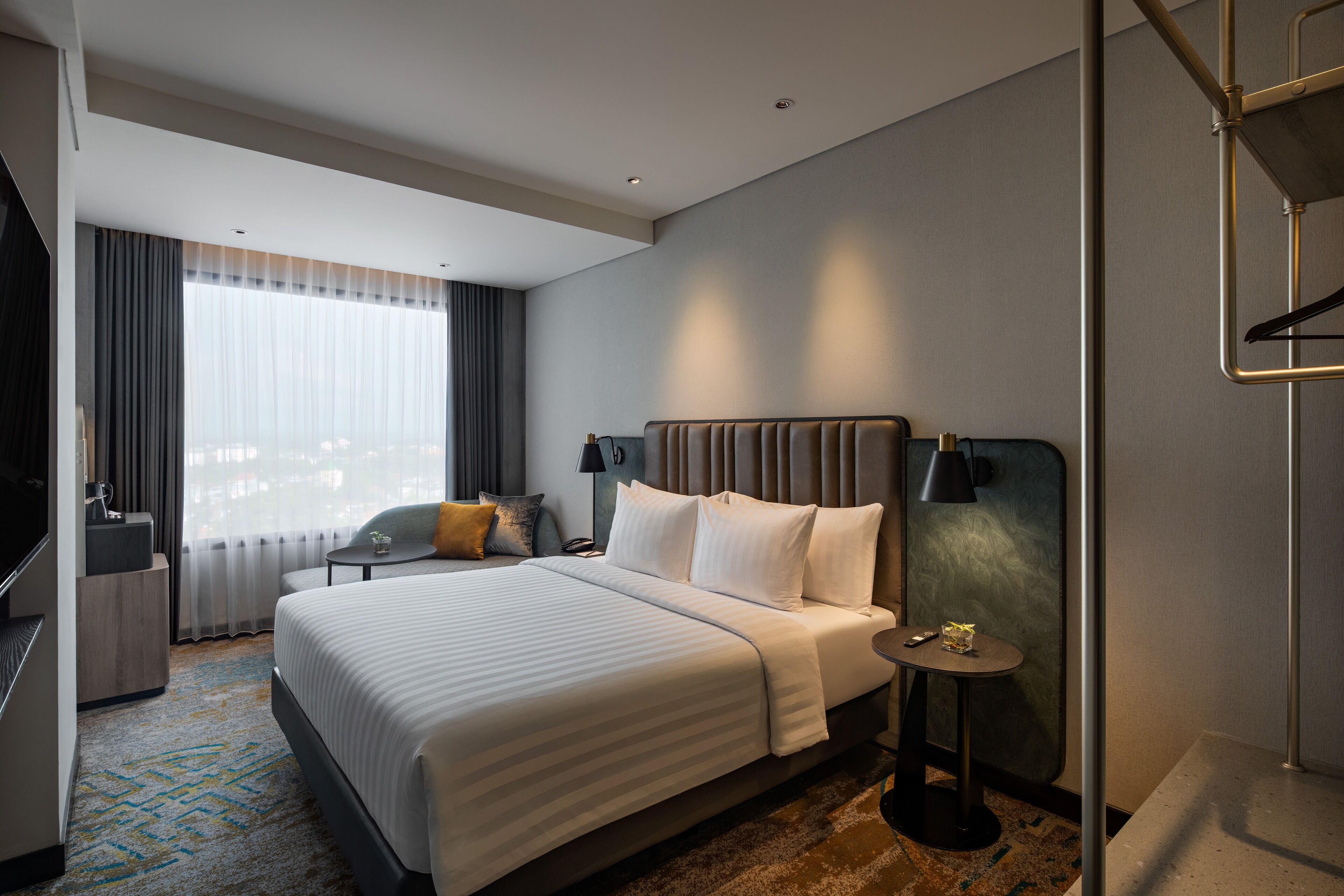 A modern hotel room with a large bed, bedside tables, a desk, and a window with curtains.