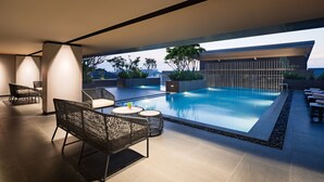 A modern outdoor pool area with seating and a view of the city skyline. - Mercure Madiun (Madiun)