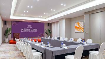 A conference room with a long table, white chairs, and a presentation screen.