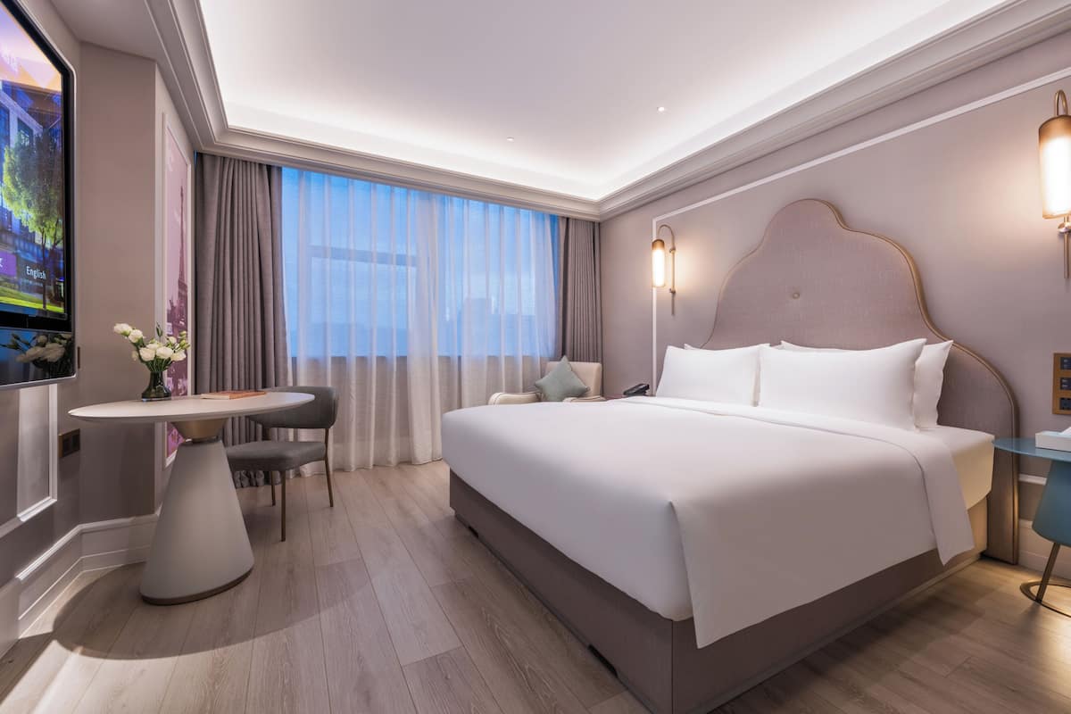 A hotel room with a large bed, a desk, a chair, a TV, and a window with curtains.