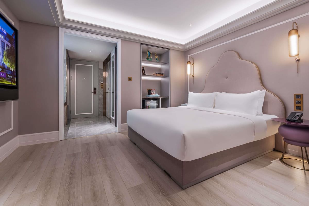 A modern hotel room with a large bed, a television, a desk with a phone, and a bookshelf.