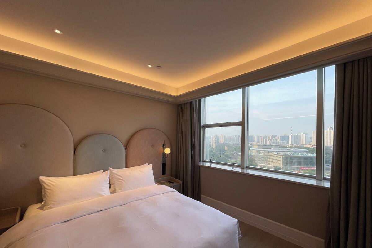 A hotel room with a large bed, a city view, and a modern design.