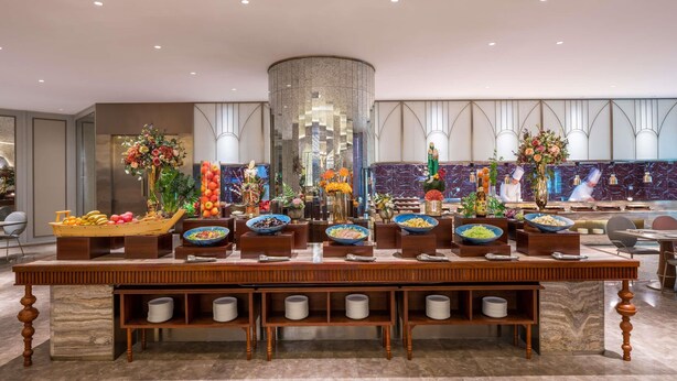 A buffet setup with various food bowls, a central decorative pillar, and a modern kitchen in the background. - Mercure Shijiazhuang People Square (Shijiazhuang)