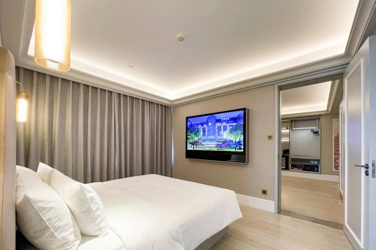 A hotel room with a bed, curtains, a television, and a mirror.