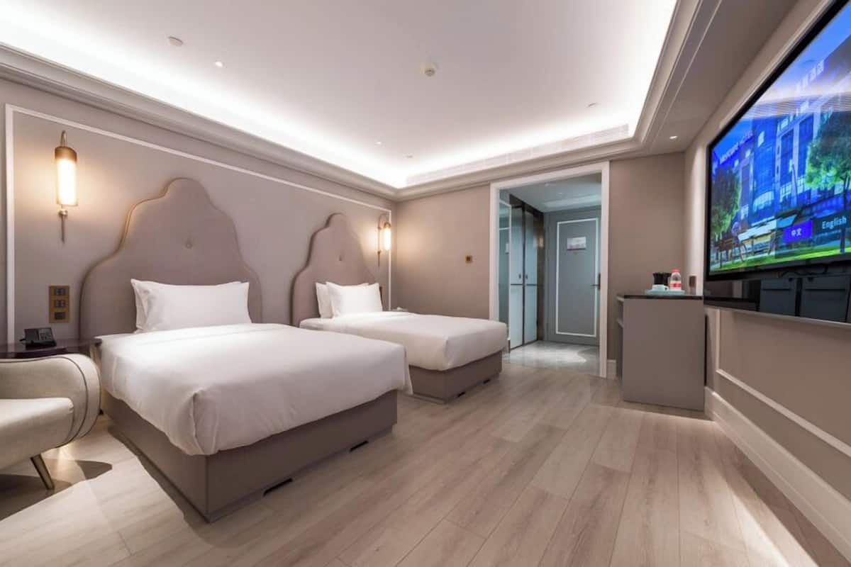 A hotel room with two beds, a TV, a desk, and a chair.