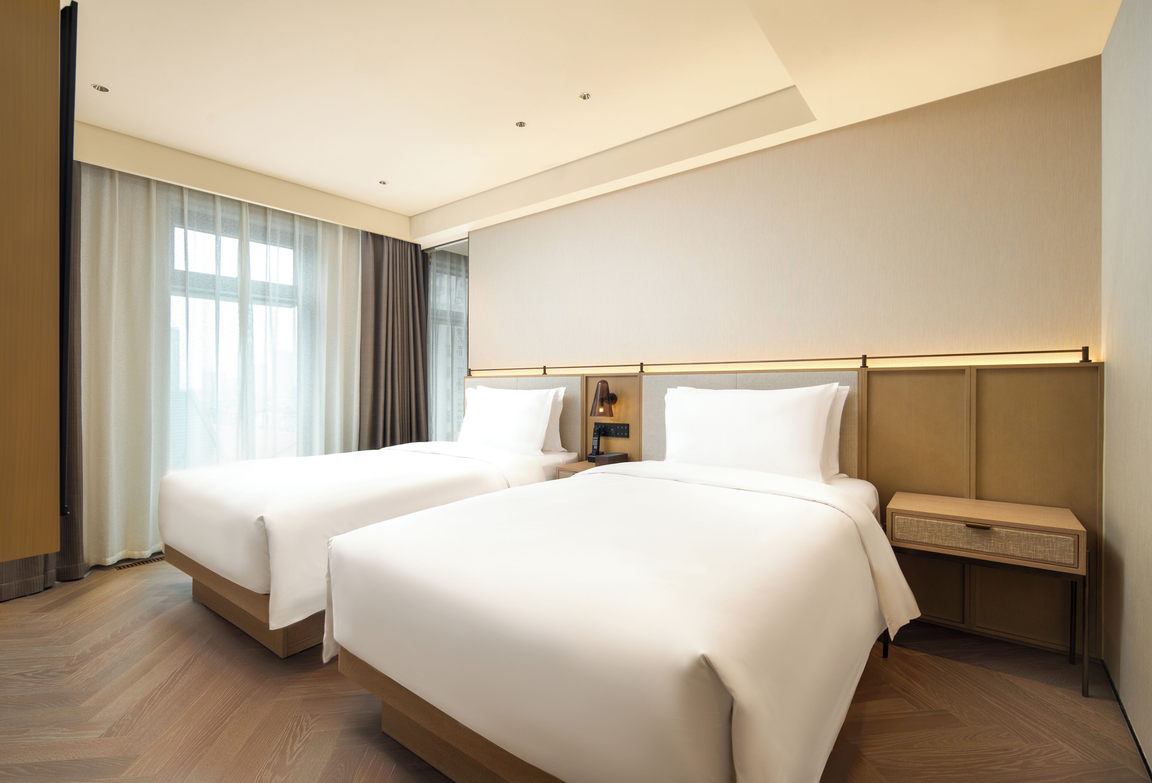 A hotel room with two beds, a nightstand, and a large window with curtains.