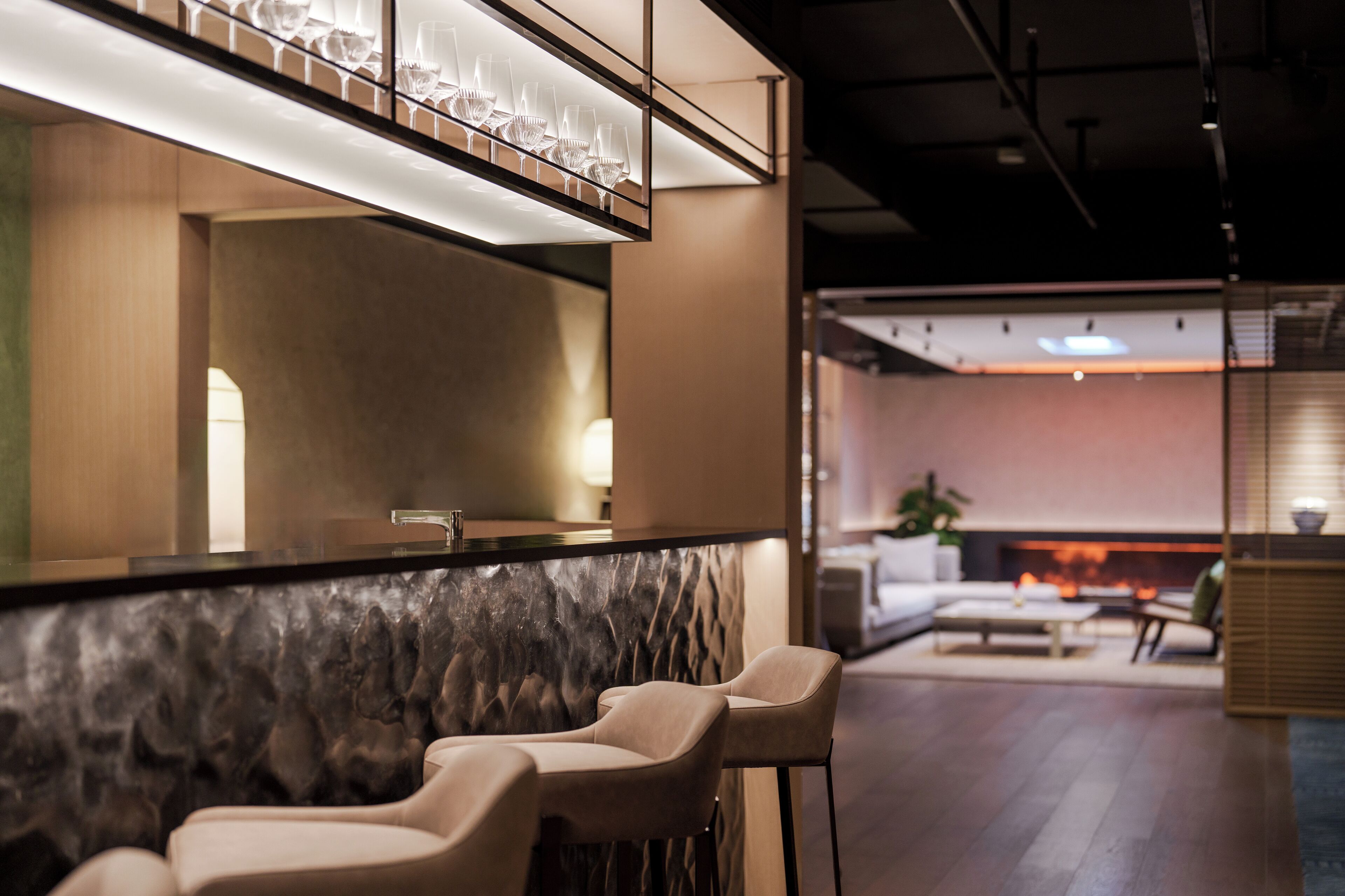 A modern bar area with a marble countertop, bar stools, and a glass display.