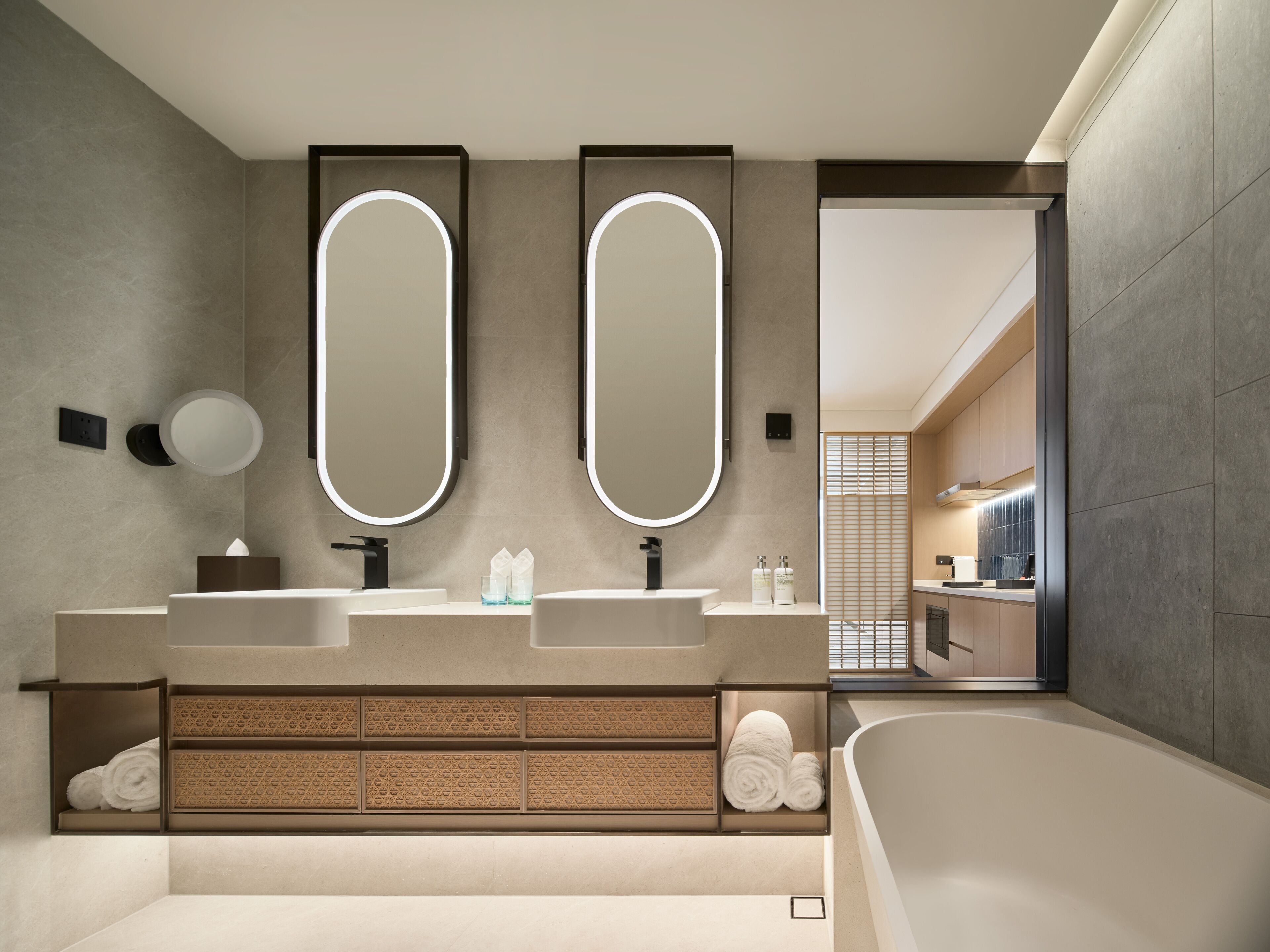 Une salle de bain moderne avec deux grands miroirs, une baignoire et un meuble-lavabo doté d’une étagère intégrée pour les serviettes.