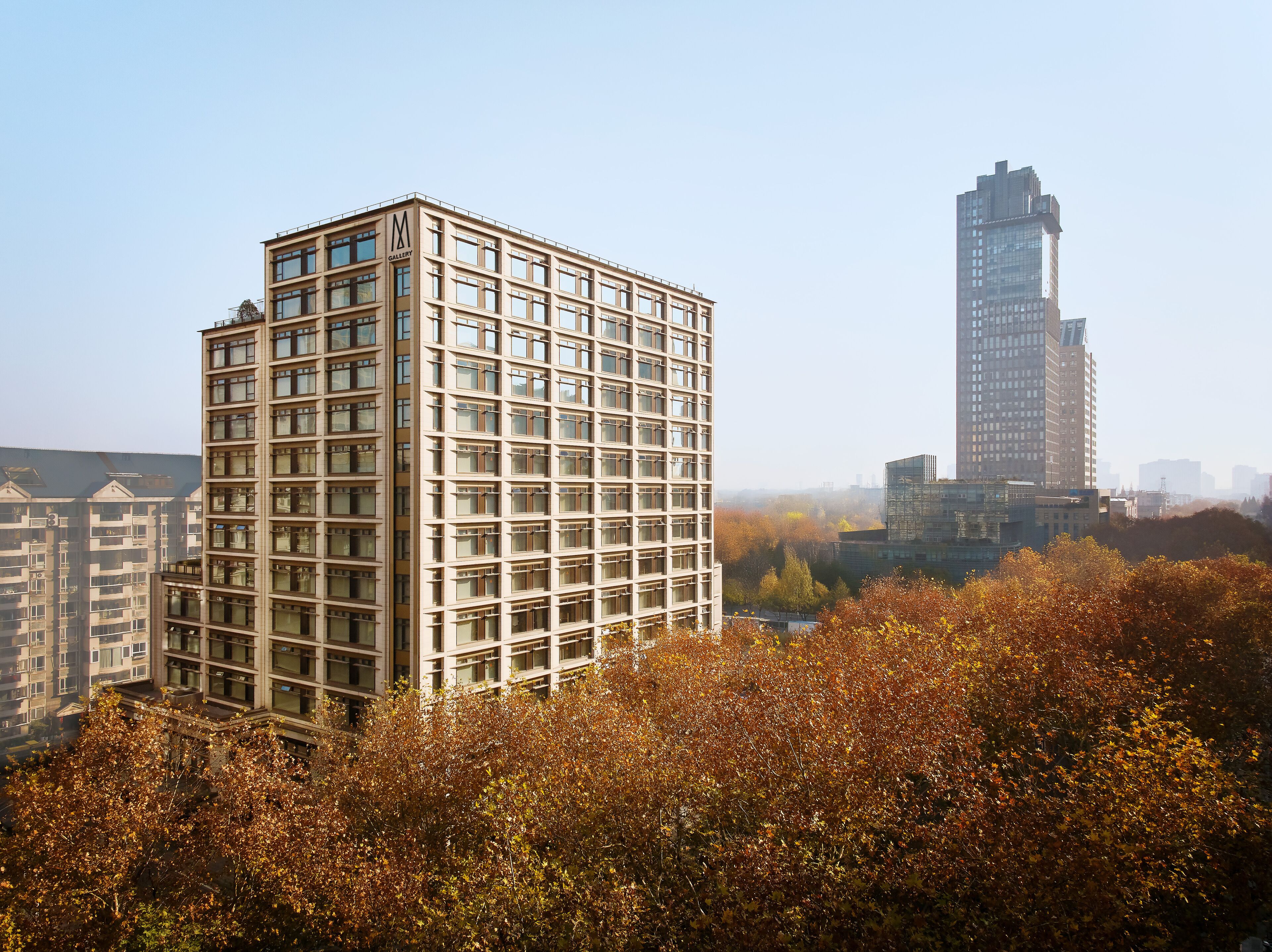 A modern high-rise building with a grid of windows and a prominent 'M' logo on the facade.