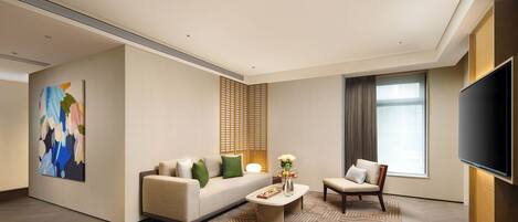 A modern living room with a sofa, coffee table, and armchair, a flat-screen TV, and a large abstract painting on the wall.