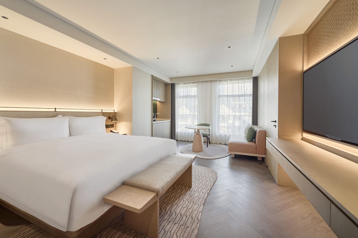 A modern hotel room with a large bed, a seating area with a table, and a TV mounted on the wall.