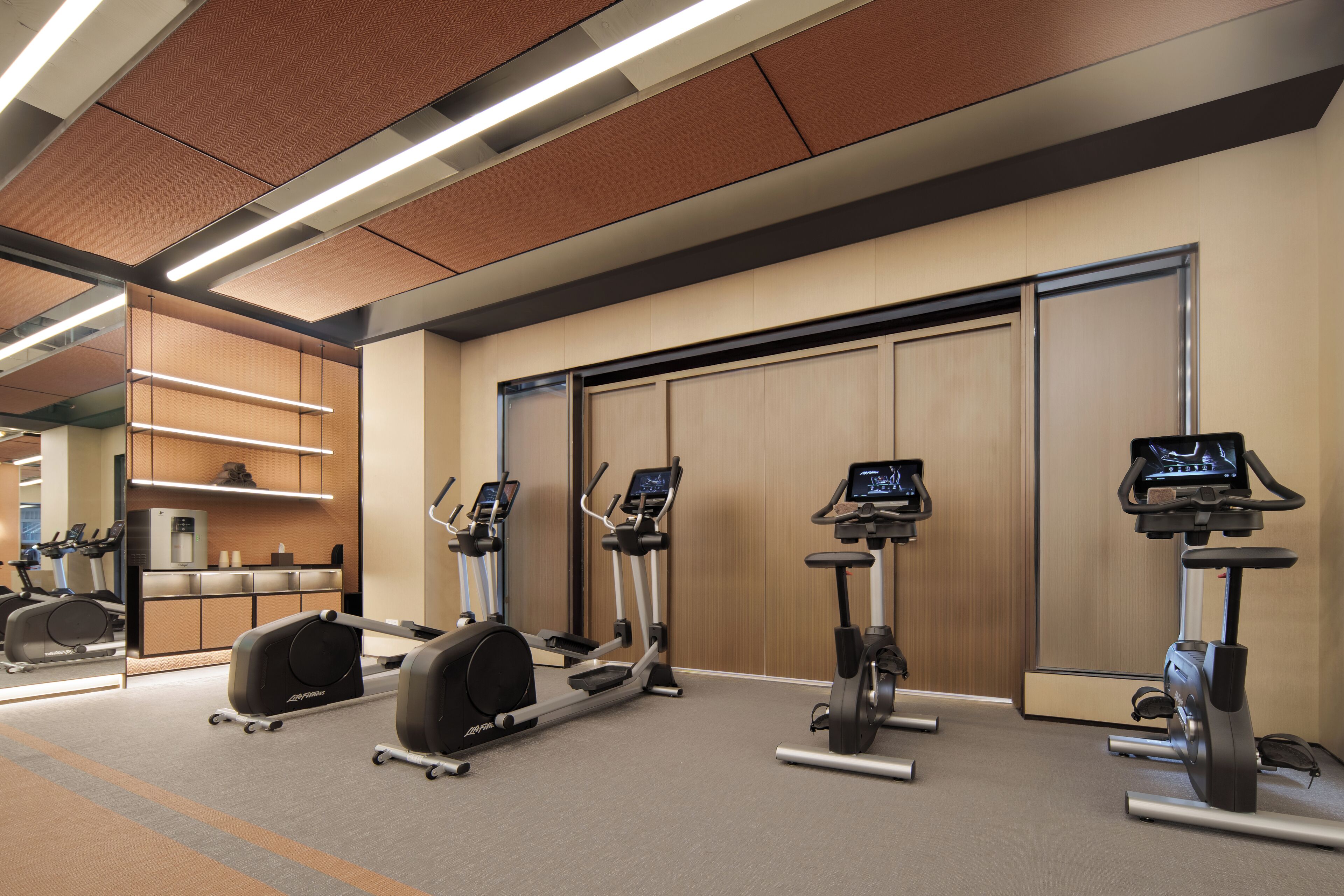 Une salle de sport équipée de tapis de course, de vélos elliptiques et d’un distributeur d’eau.