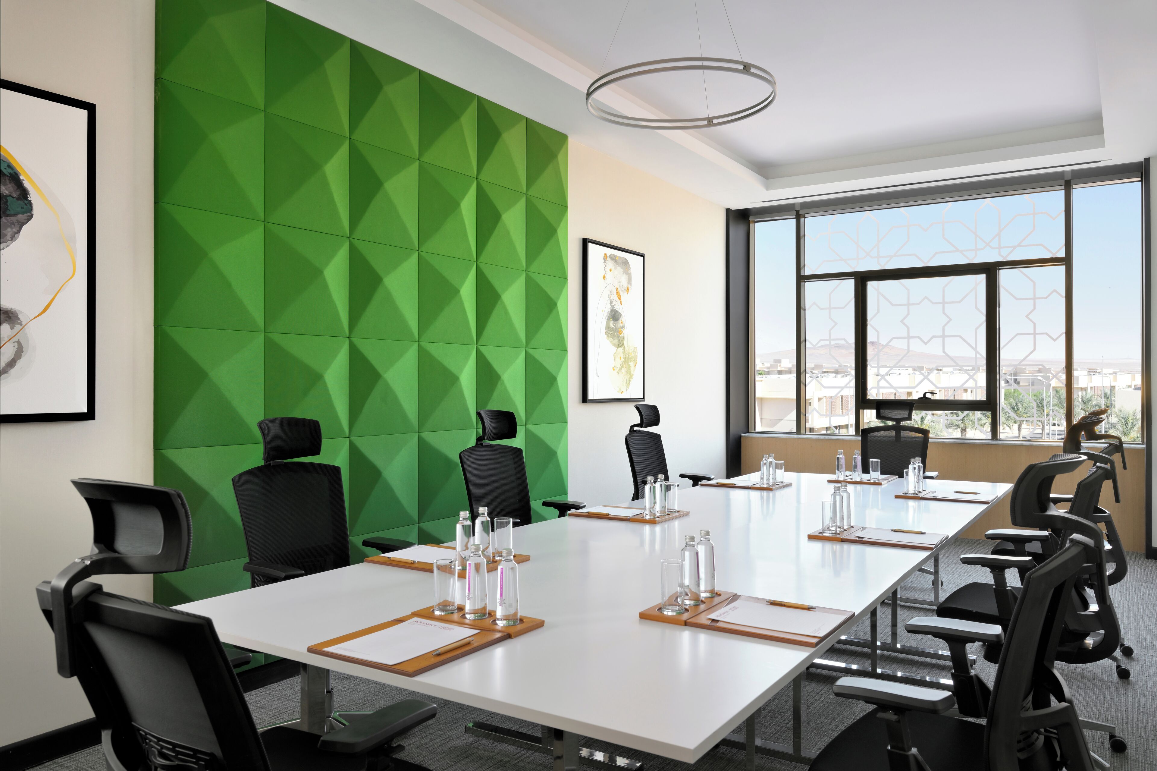 A conference room with a long table, multiple chairs, and a green geometric wall.
