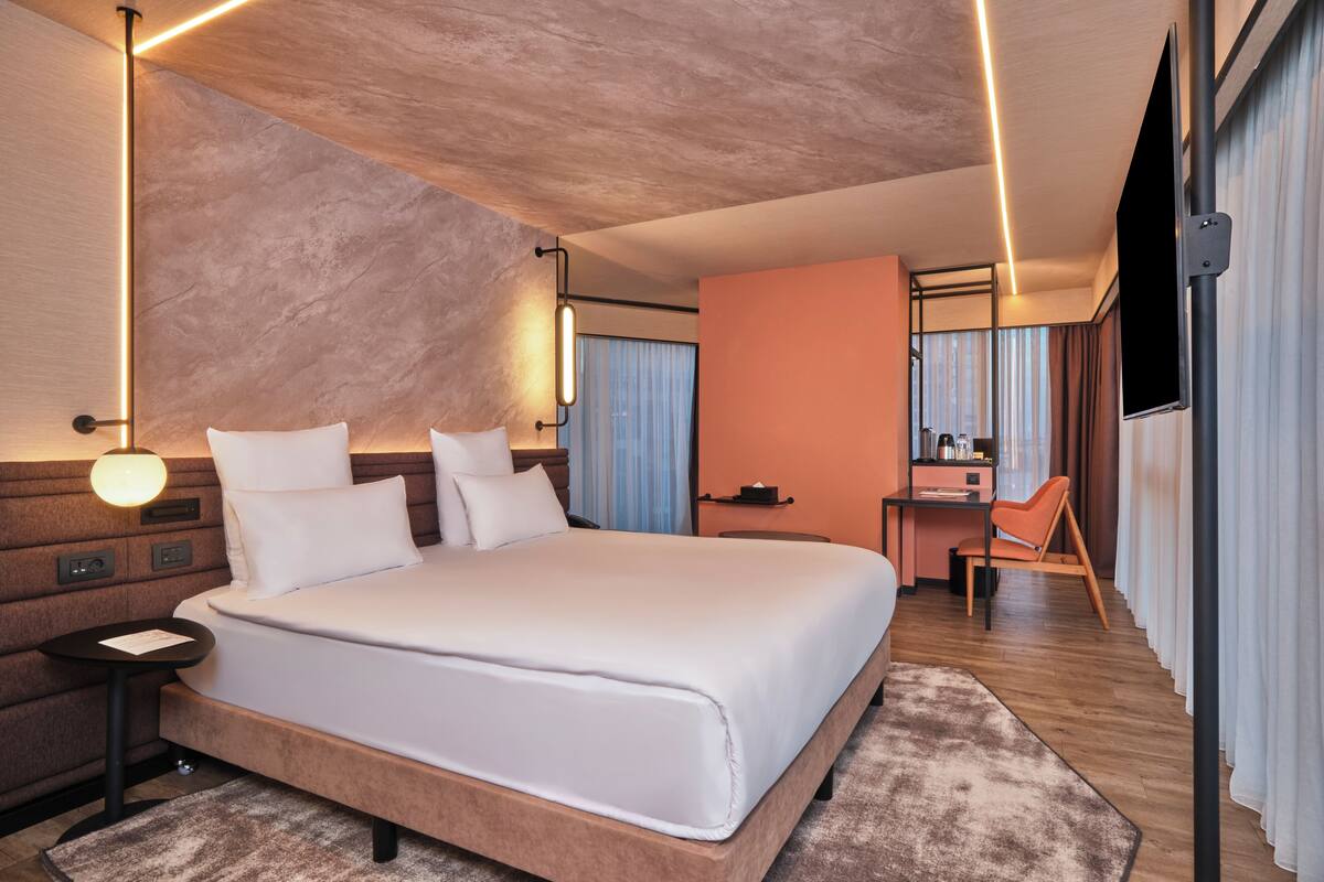 Una habitación de hotel moderna con una cama grande, mesitas de noche, un escritorio y una silla.
