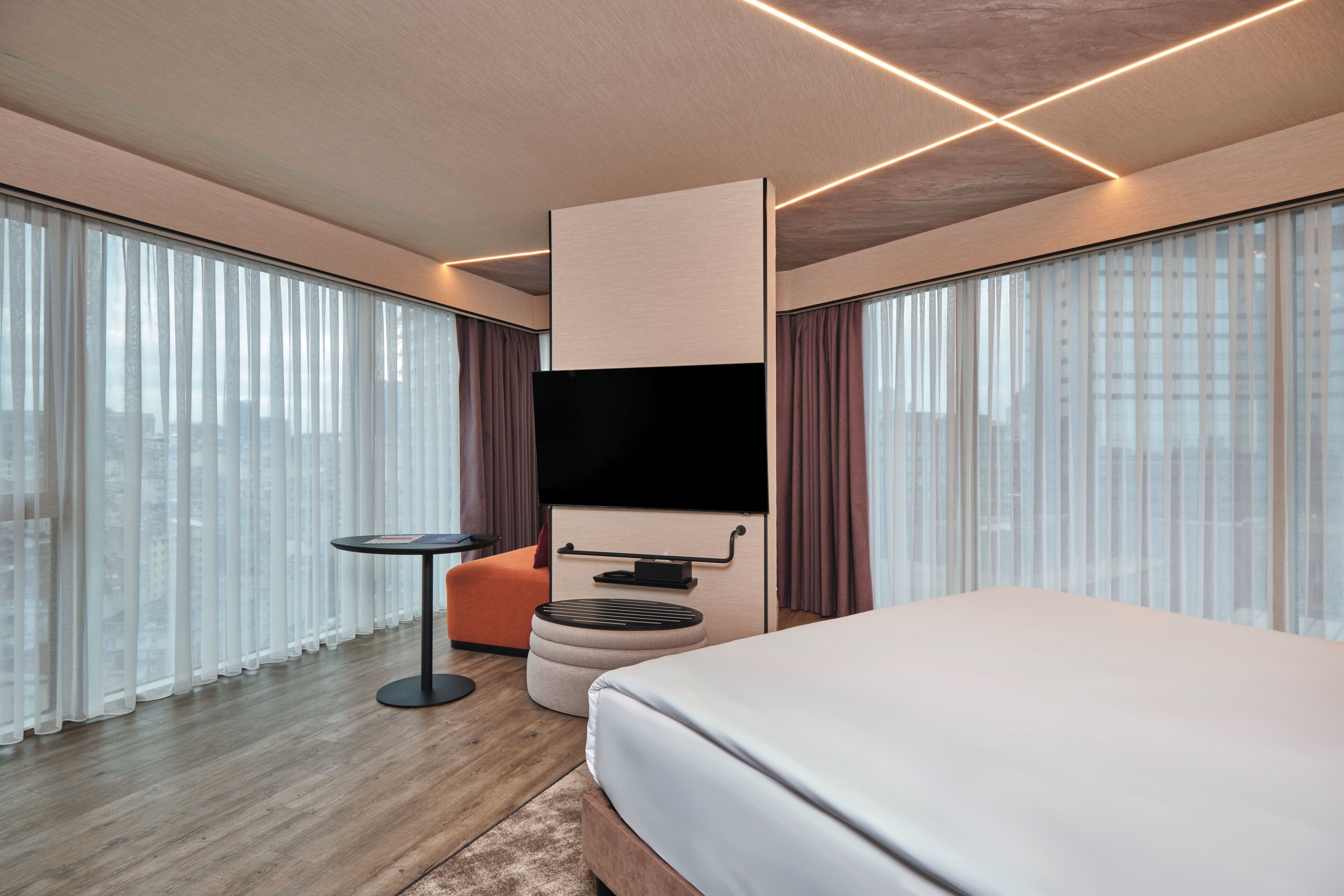 A modern hotel room with a large bed, a flat-screen TV, a small round table, and a sofa.