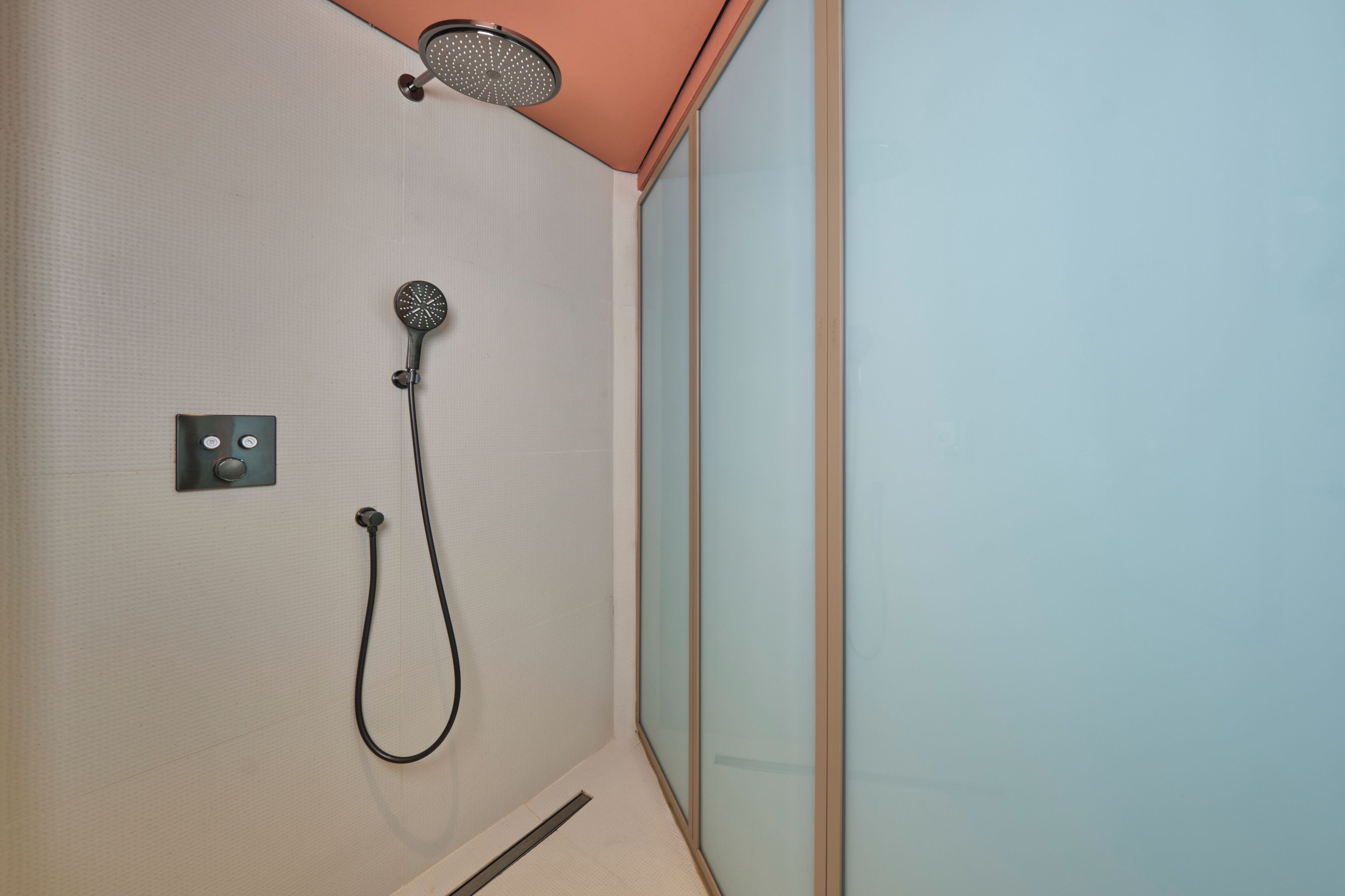 Une douche équipée d’un pommeau de douche à main et d’un panneau de commande fixé au mur.