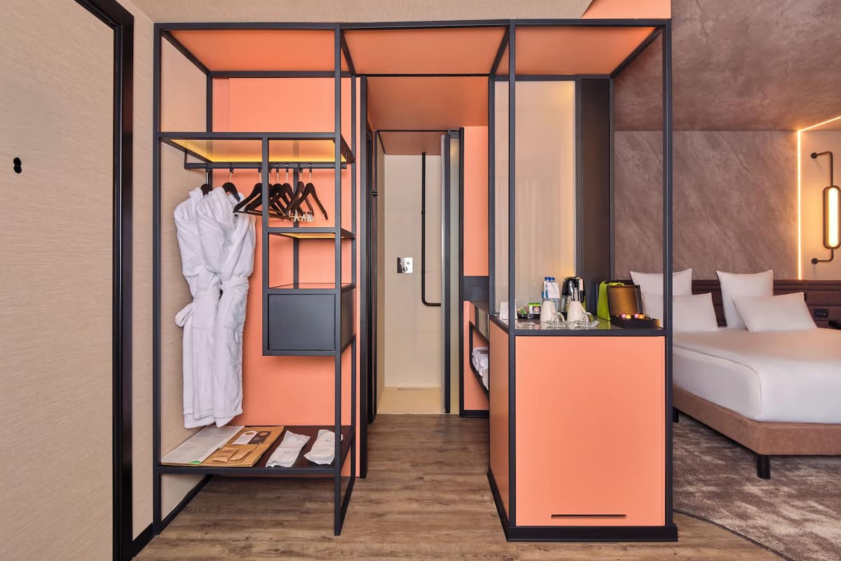 Una habitación de hotel con cama, escritorio con lámpara, armario y bata colgada.