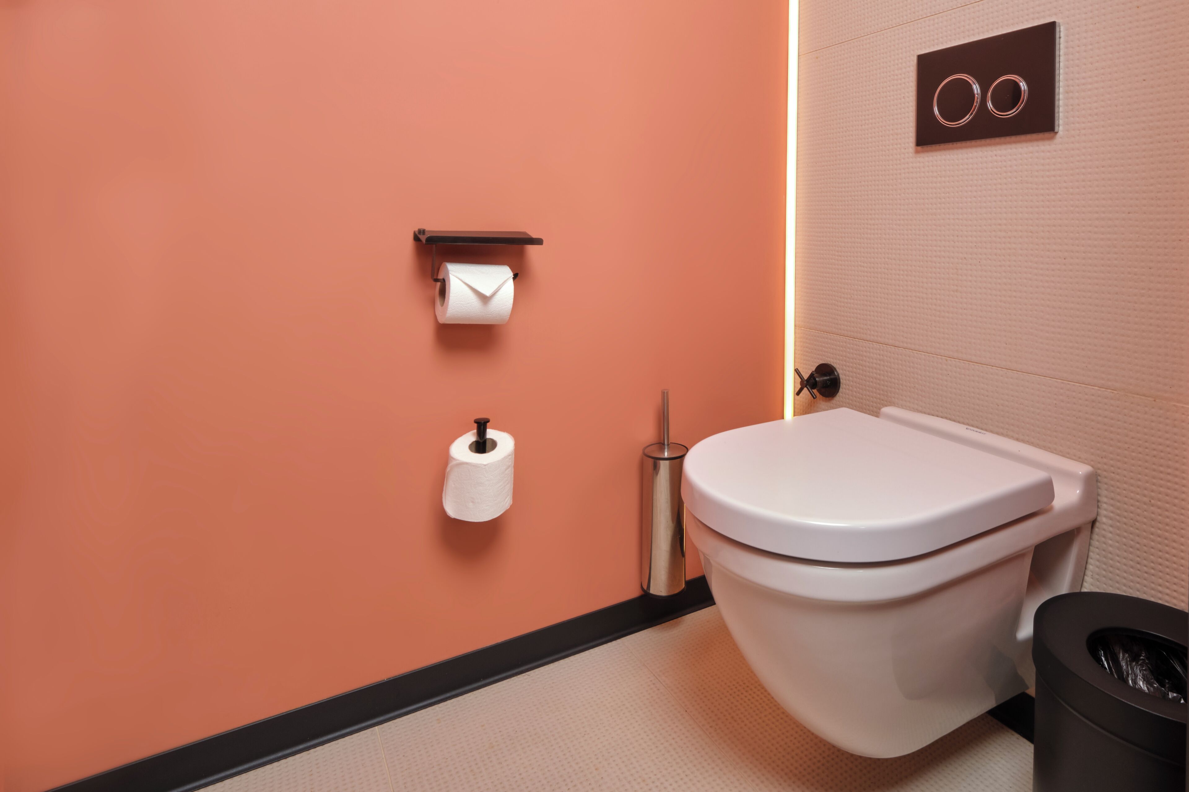 A modern bathroom with a toilet, a trash bin, and two rolls of toilet paper on the wall.