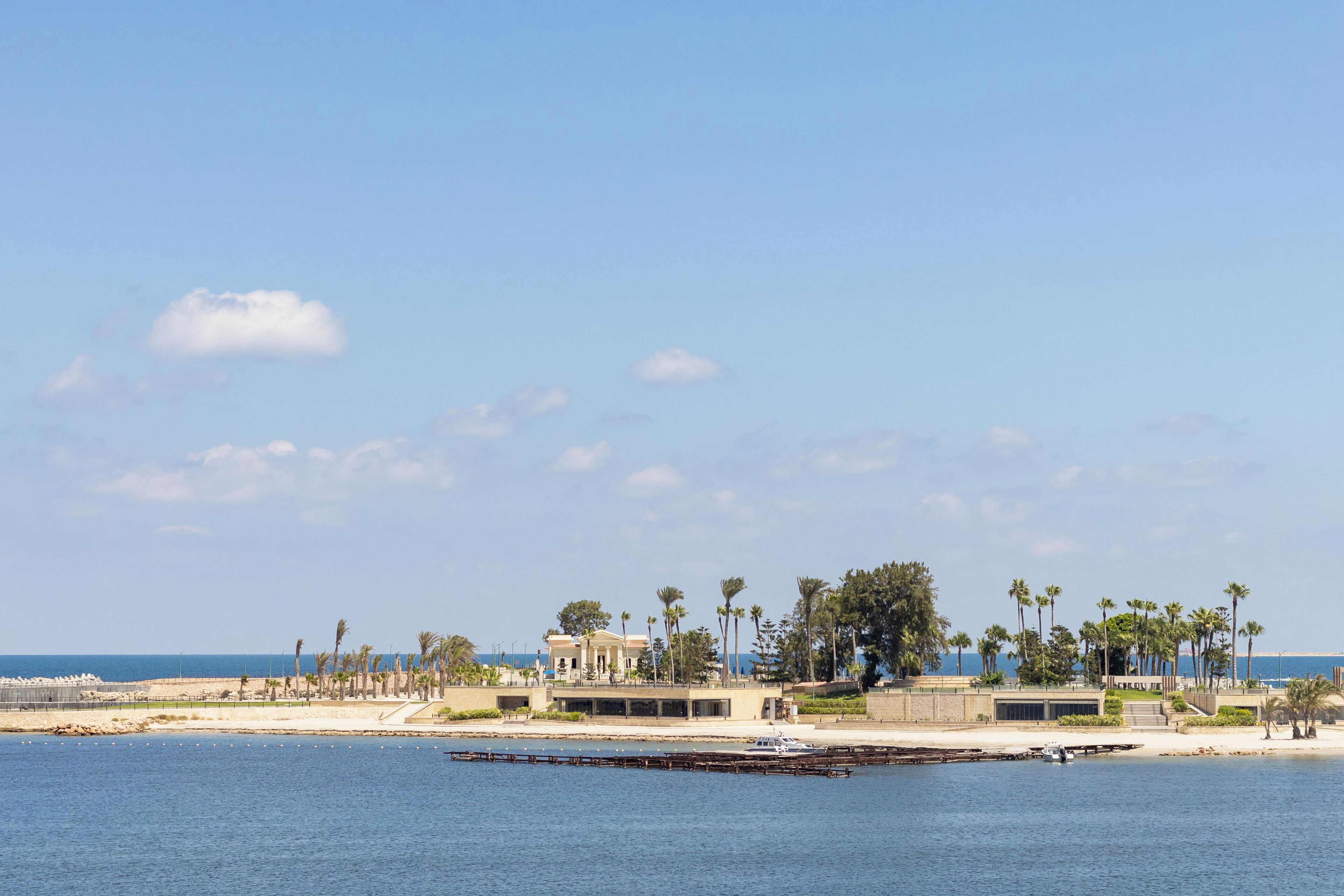 A coastal hotel with a marina, palm trees, and a clear view of the sea.