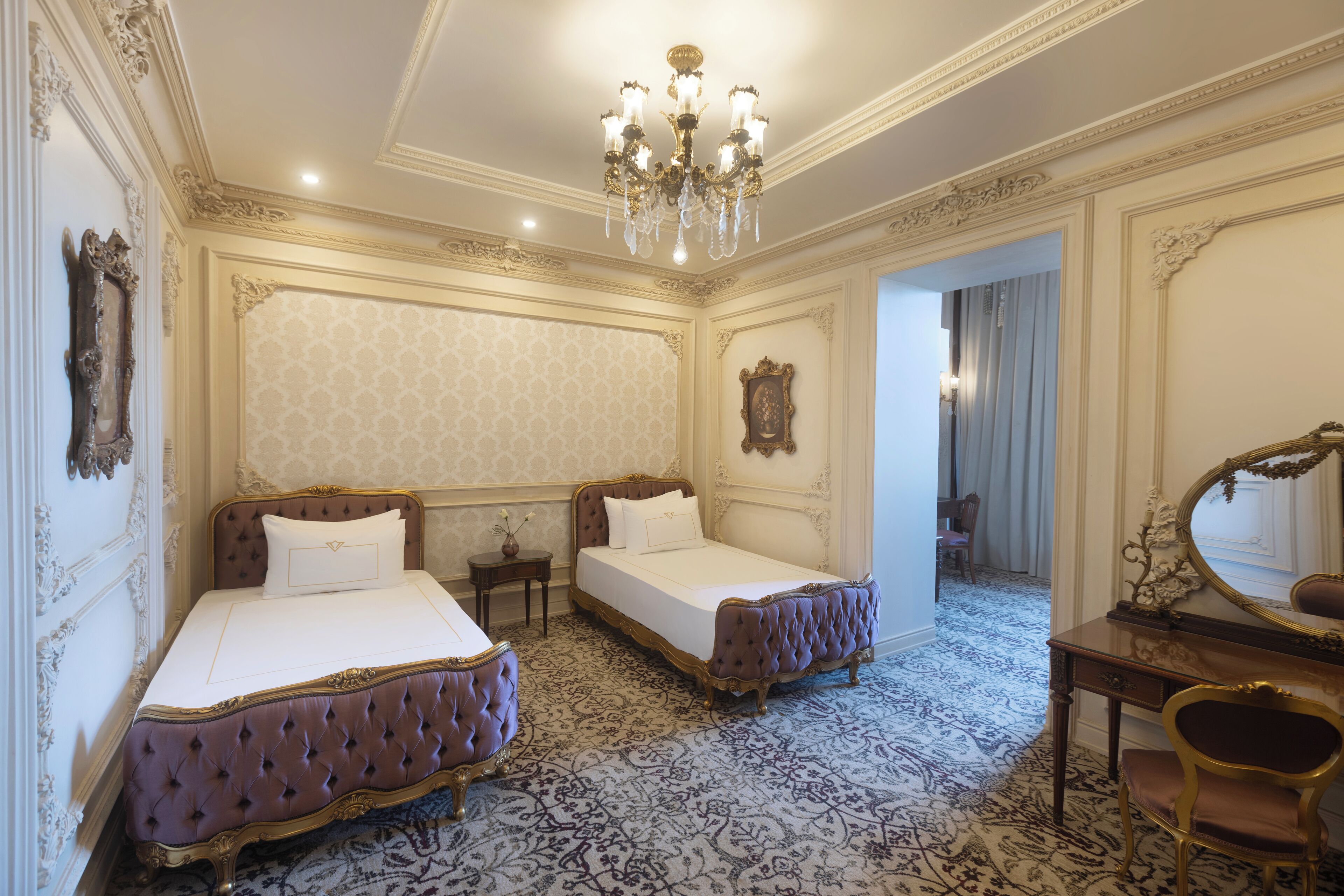 A luxurious bedroom with two beds, ornate furniture, and a chandelier.