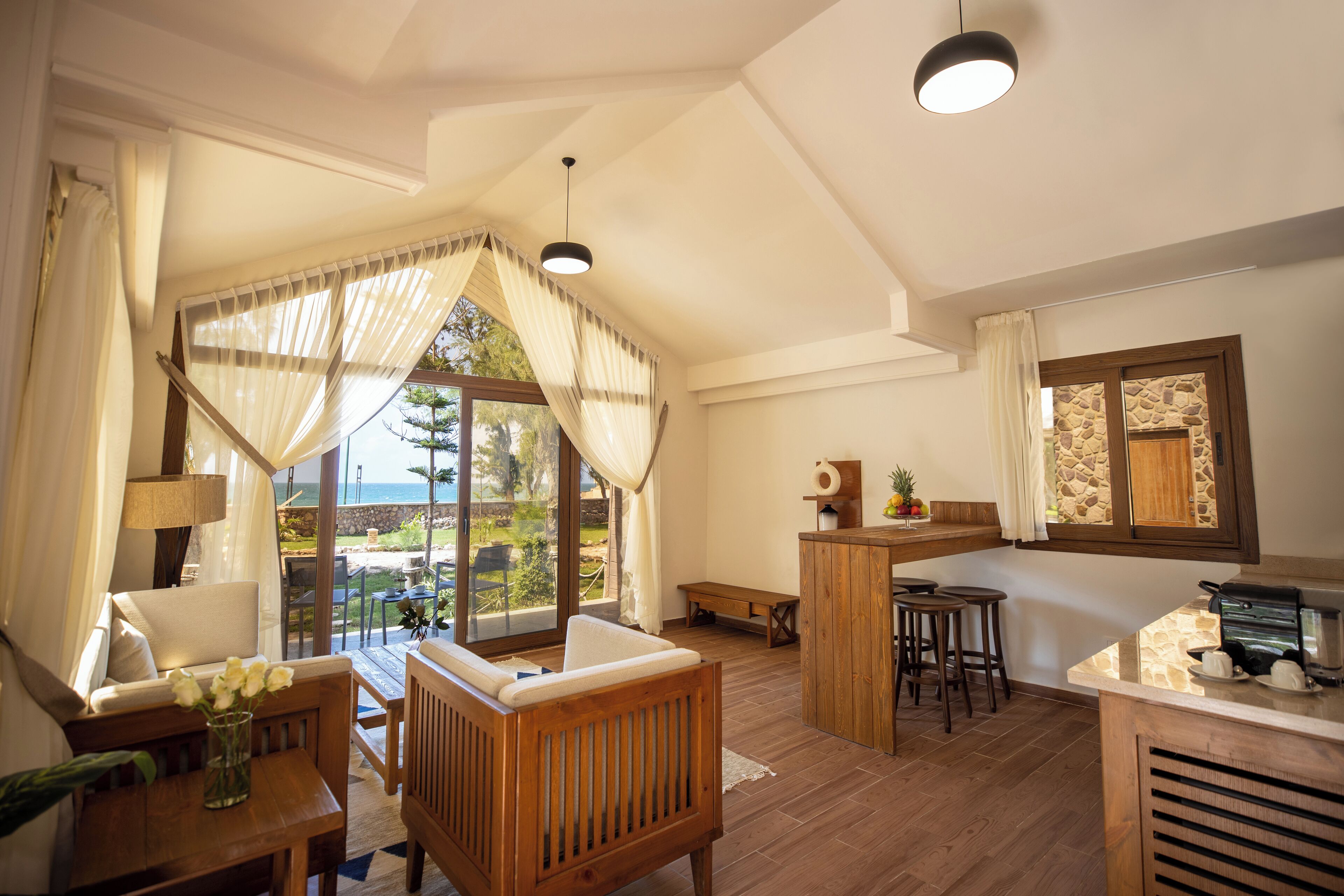 Una habitación acogedora con un banco de madera, una mesita con un florero, una zona de bar con taburetes y un ventanal con vistas al exterior.