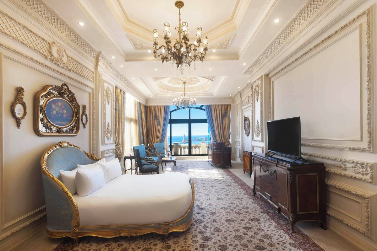 A luxurious bedroom with a large bed, a television, and a view of the sea through a large window.