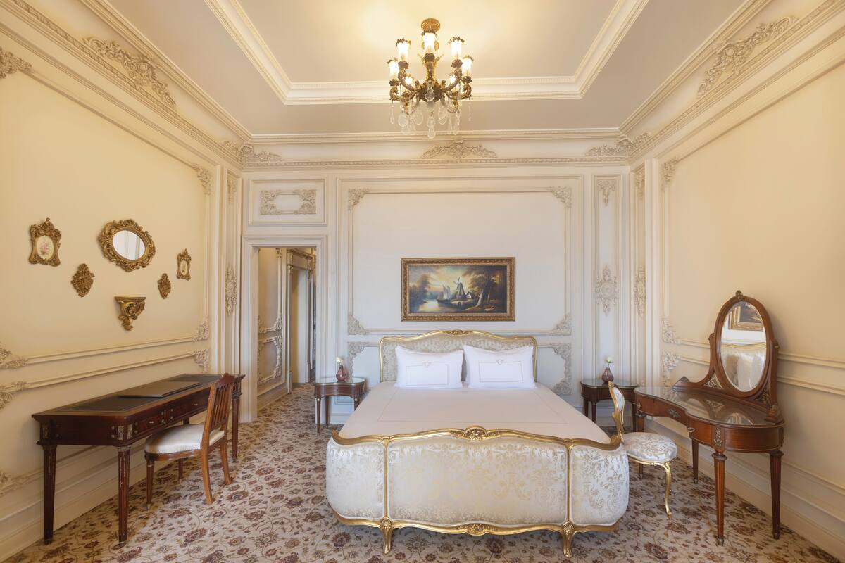A luxurious bedroom with a large bed, ornate furniture, and a chandelier.