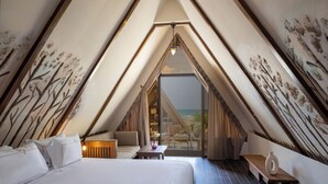 A bedroom with a large bed, a small table, and a bench. There is a view of the beach through a large window. - Rixos Montaza Alexandria (Alexandria)