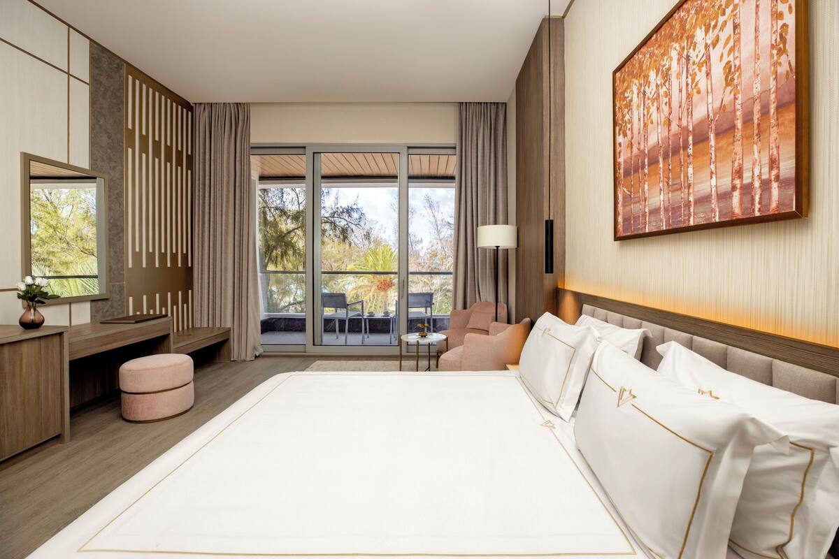 A modern hotel room with a large bed, a desk, a chair, and a view of the outdoors.