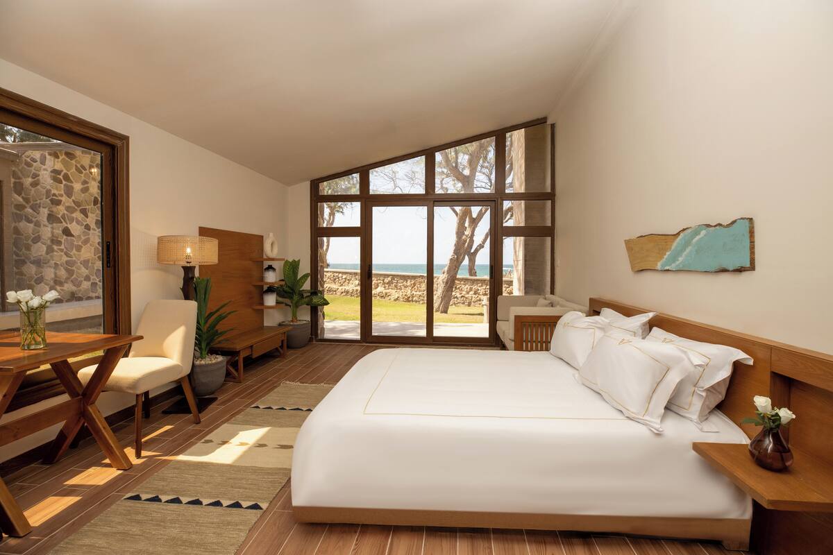 A bedroom with a large bed, a desk, a chair, and a view of the beach.