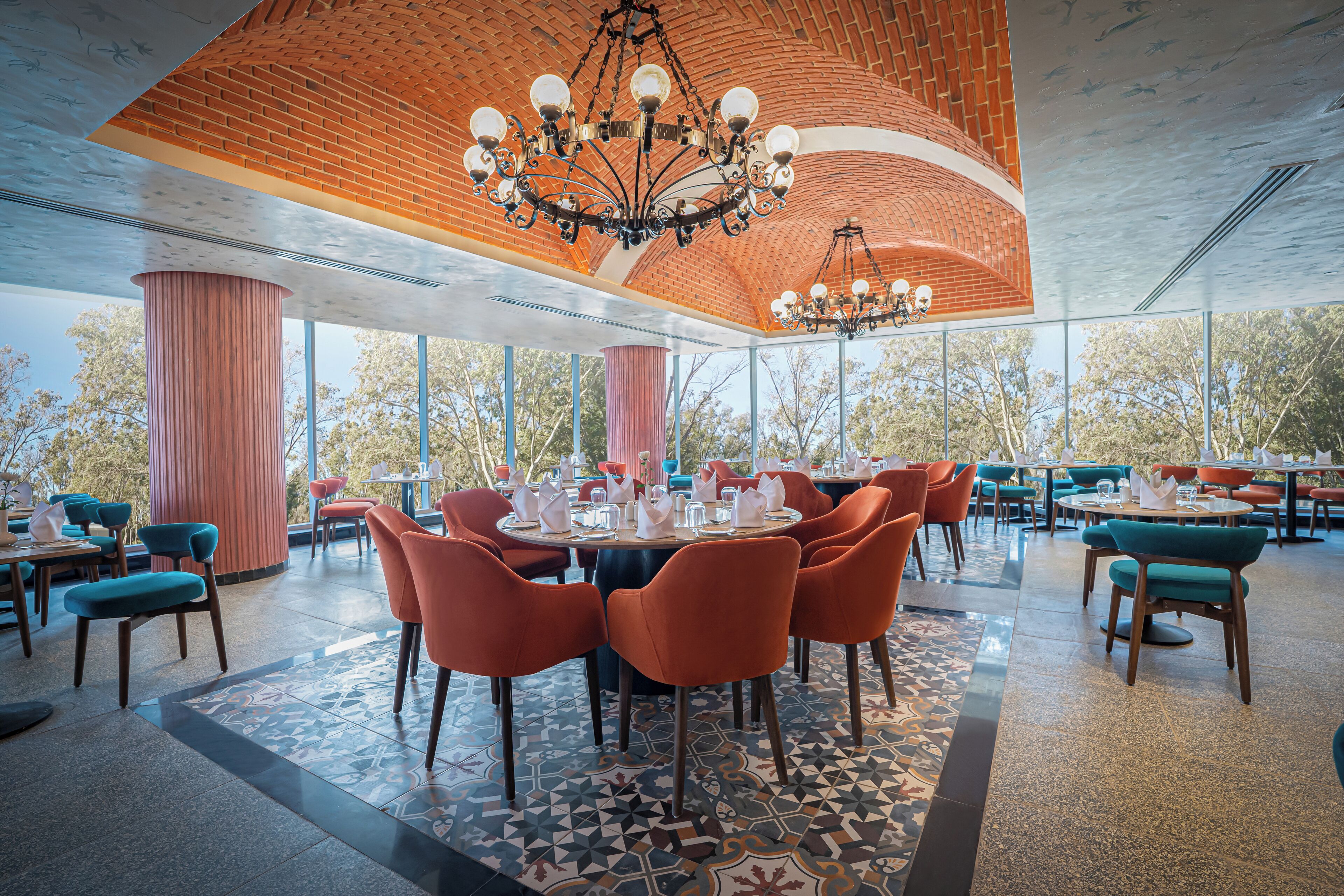 Een ruime eetruimte met ronde tafels, oranje stoelen en een grote kroonluchter.