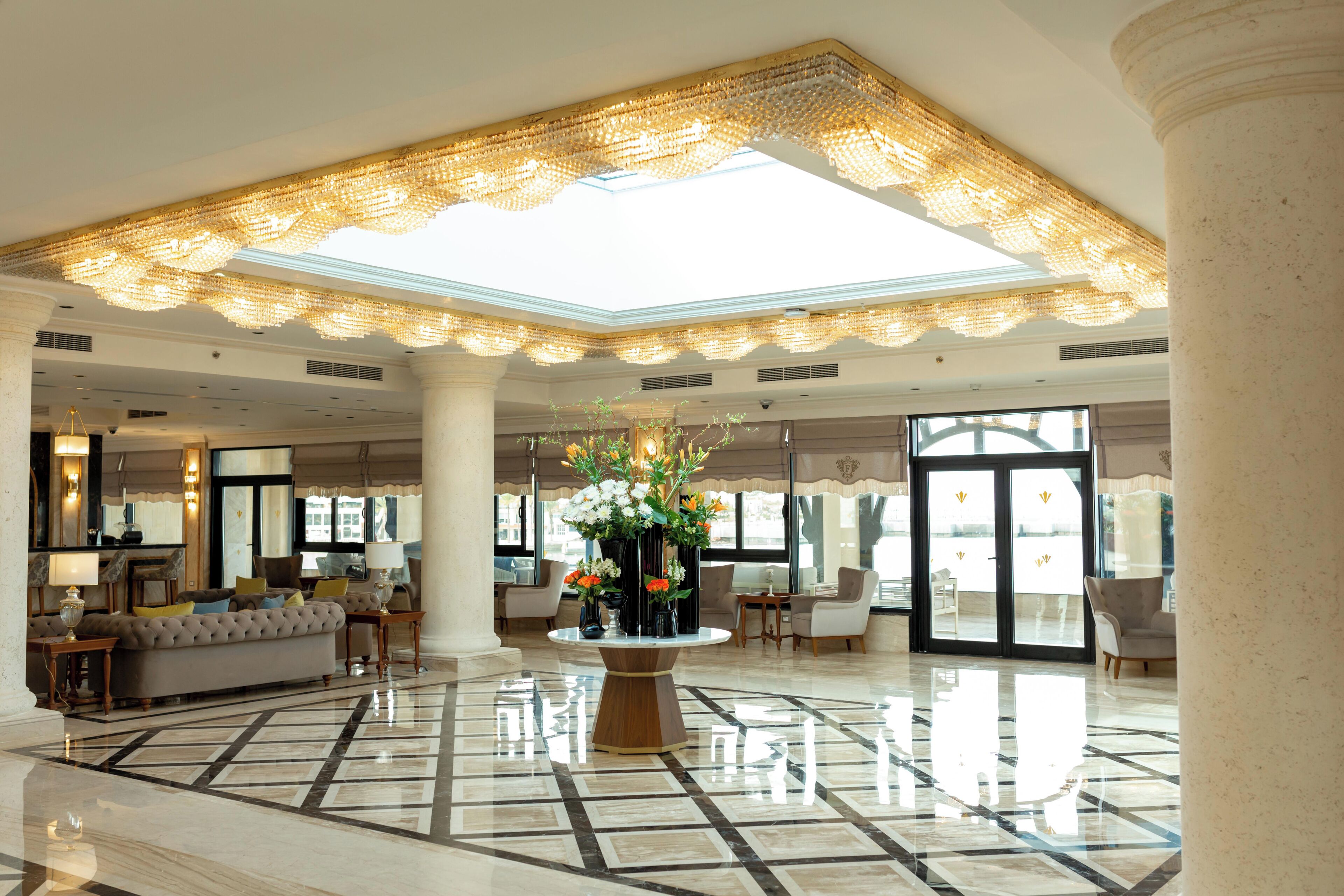 A spacious lobby with a high ceiling, a central floral arrangement, and a polished marble floor.