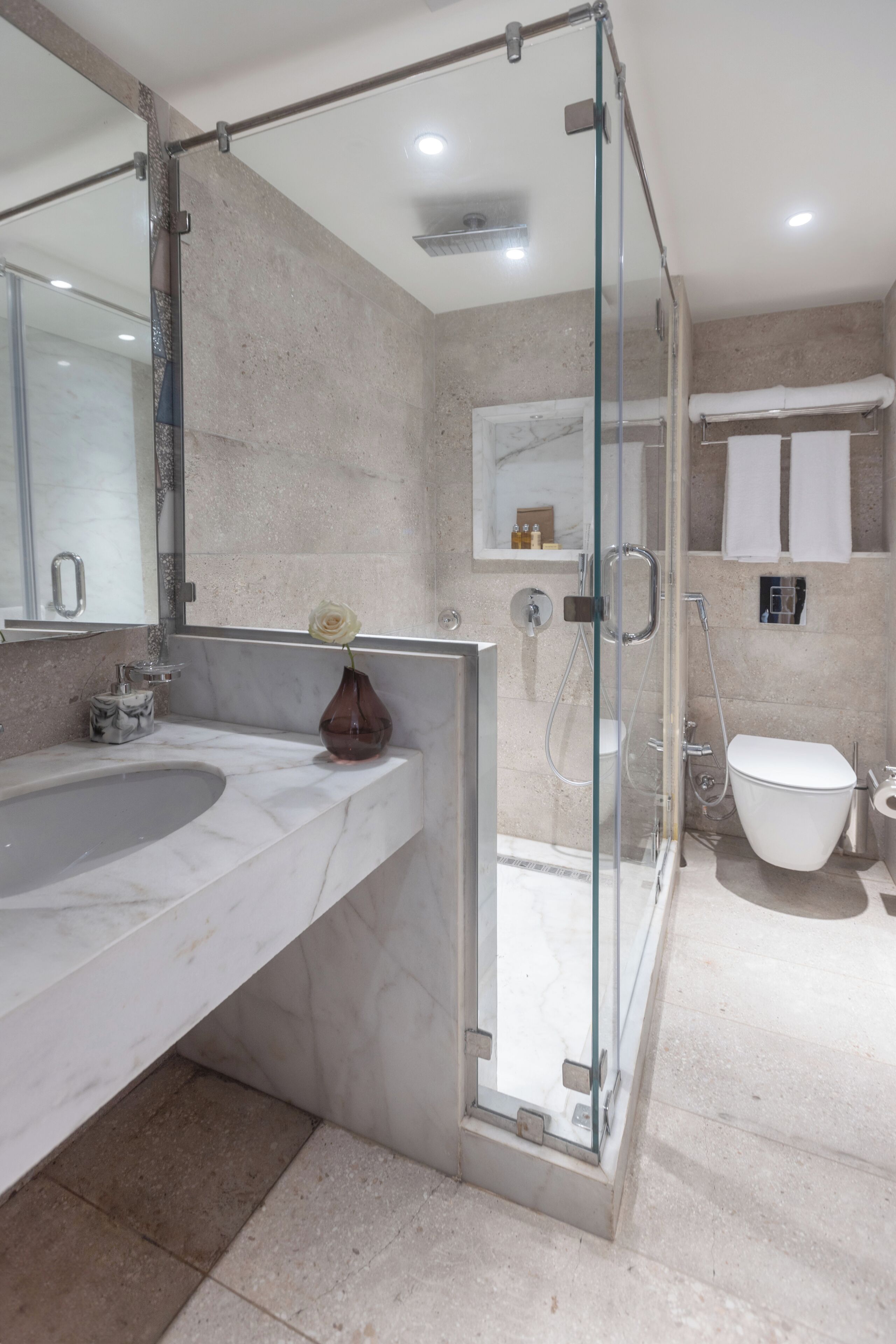 Un baño moderno con cabina de ducha de vidrio, lavamanos de mármol y retrete blanco.