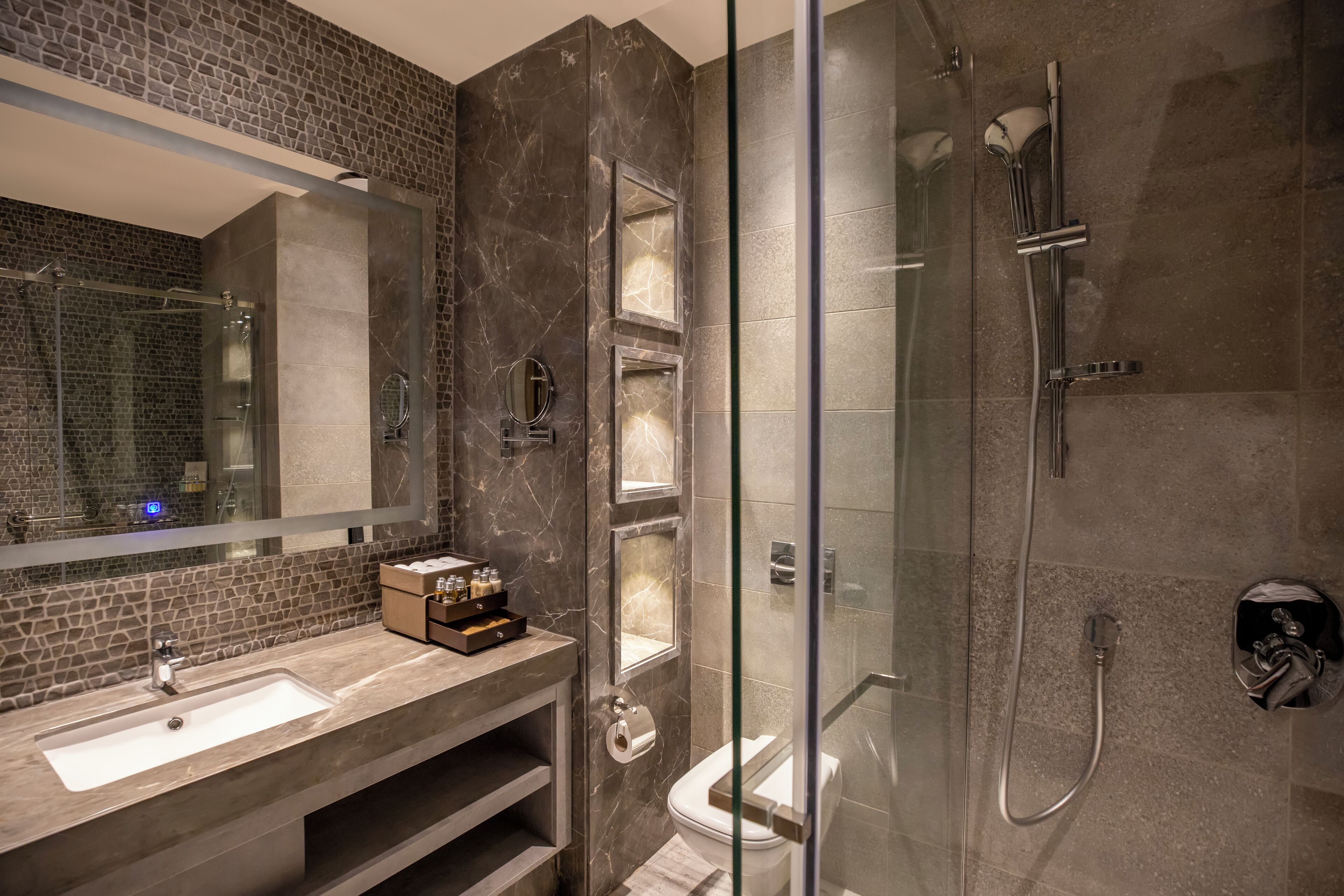 A modern bathroom with a glass-enclosed shower, a large mirror, and a marble backsplash.