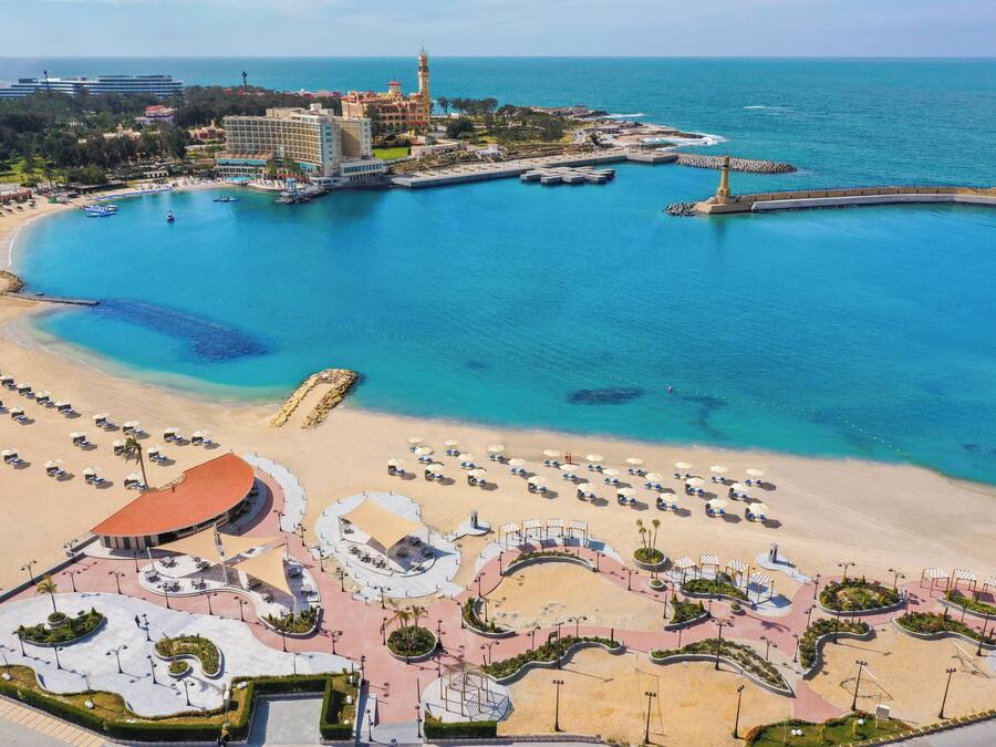 Ein Küstenort mit einem breiten Sandstrand, einer Marina und einem markanten Gebäude mit einem Turm.