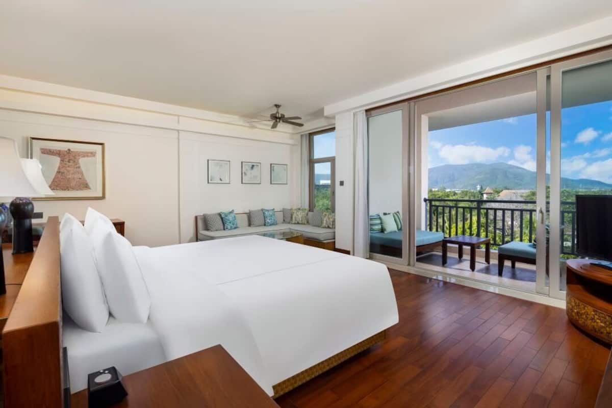 Een slaapkamer met een groot bed, een slaapbank en een balkon met uitzicht op bergen.