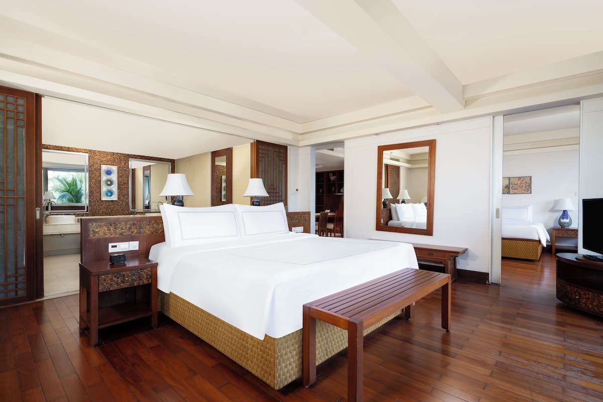 Hotelkamer met een groot bed, houten vloer, een bureau met stoel, een televisie en een badkamer door een open deur zichtbaar.