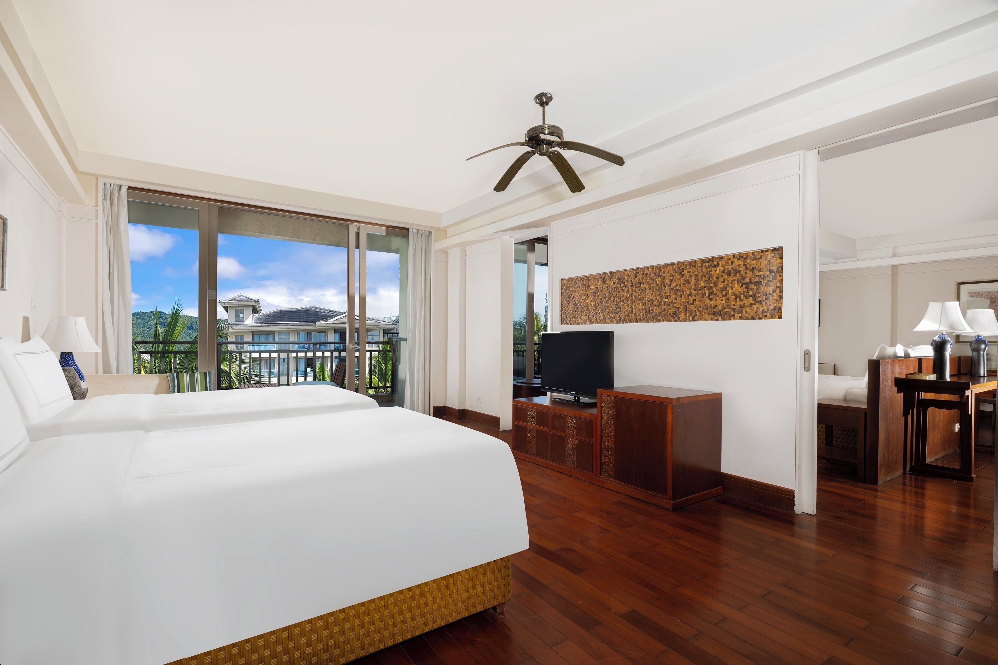 Een hotelkamer met een groot bed, een plafondventilator, een televisie en een balkon met uitzicht op de bergen.