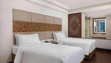 Two comfortable beds with white linens and a headboard feature in this stylish room, complemented by a wooden partition and large mirror.