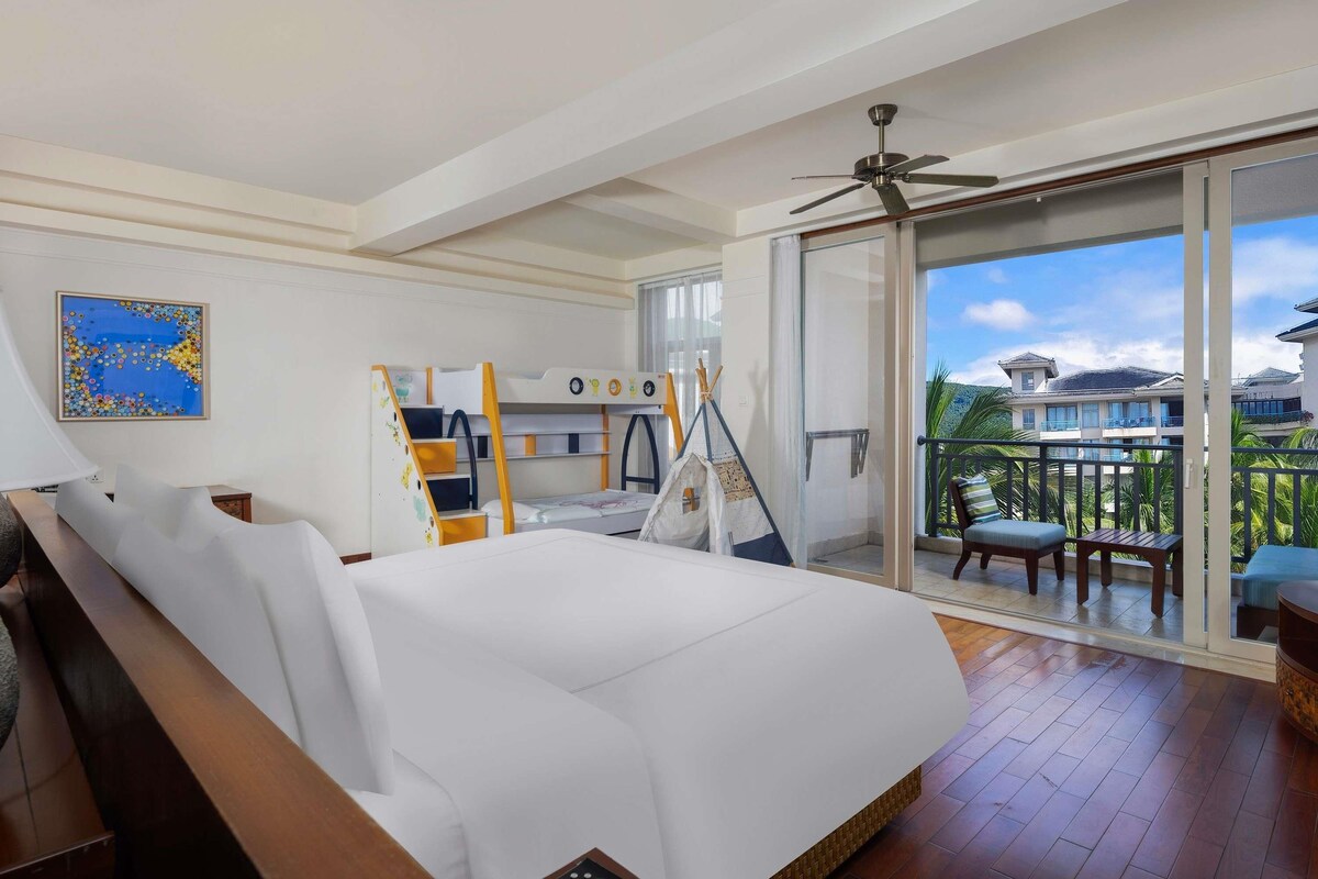Een hotelkamer met een bed, een bureau, een stoel, een balkon met uitzicht en een plafondventilator.
