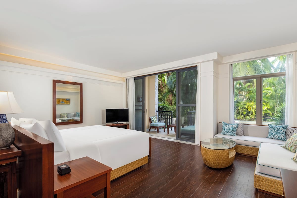 Een hotelkamer met een bed, een televisie, een bank, een glazen tafel en een balkon met stoelen.