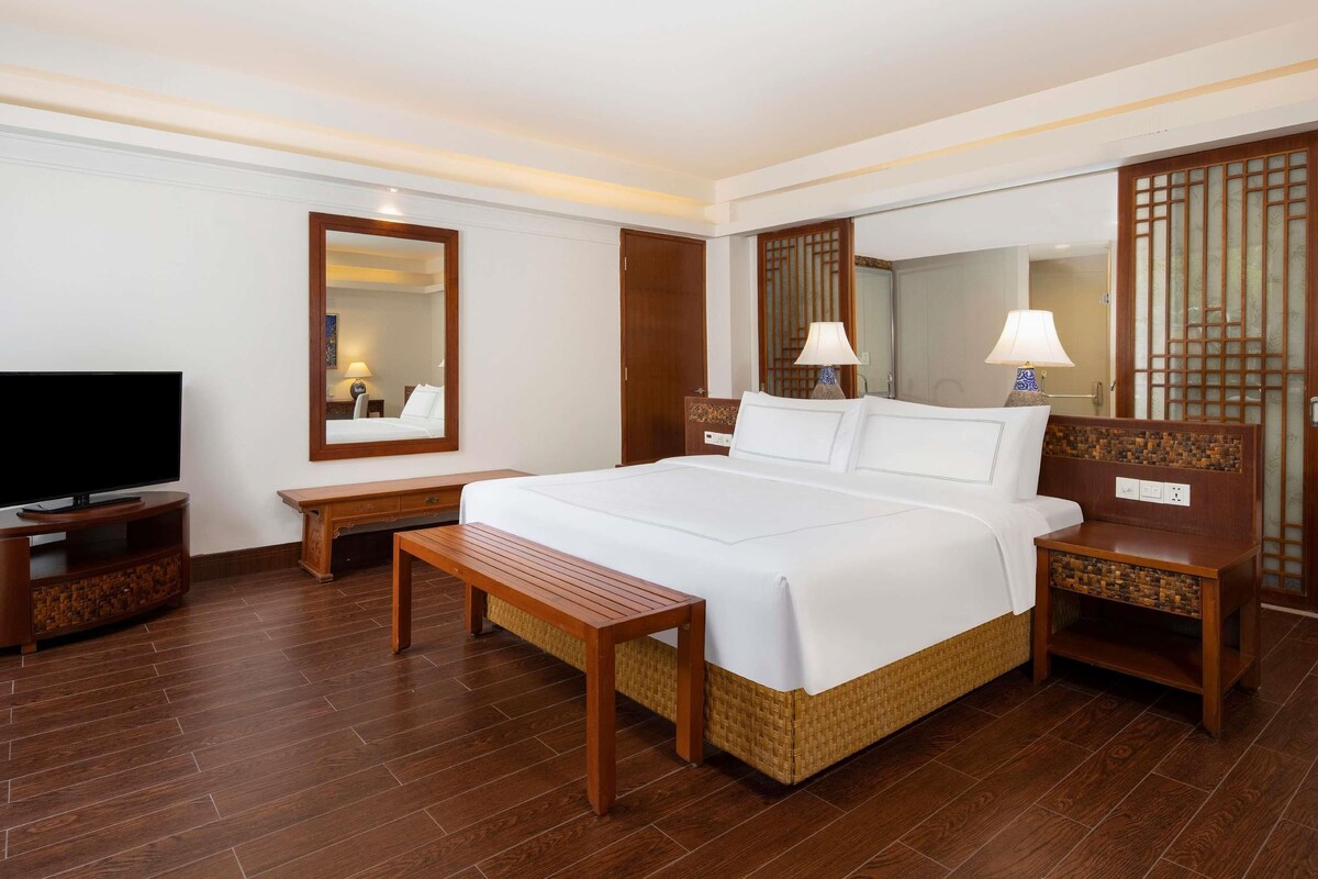 Een hotelkamer met een groot bed, een televisie, een houten bankje en een bureau met een lamp.