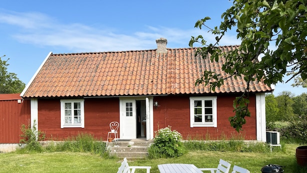 Et rødt hus med tegltag, en fordør og en lille veranda med en stol.