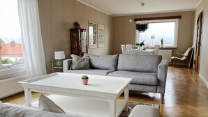 A living room with a grey sofa, white coffee table, and a small potted plant. There is a dining area with a table and chairs in the background. - Large villa with sea view in Rönnäng | SE09078 (Rönnäng)
