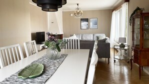 A dining area with a white table, chairs, and a vase with flowers. There is a grey sofa and a television in the background. - Large villa with sea view in Rönnäng | SE09078 (Rönnäng)