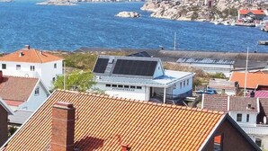 A coastal building with a red-tiled roof, a small attached structure with solar panels, and a view of the sea and wind turbines in the background. - Large villa with sea view in Rönnäng | SE09078 (Rönnäng)