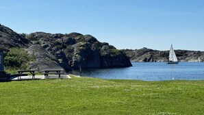 A lakeside view with a sailboat, picnic tables, and rocky hills.