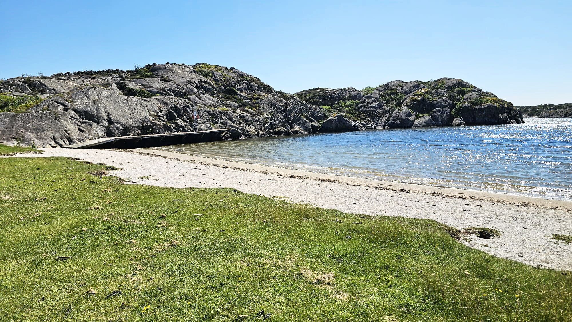 A coastal landscape with a grassy area, rocky cliffs, and a clear blue sea.
