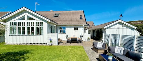 Una casa blanca con techo de tejas, patio trasero cercado y mobiliario exterior.